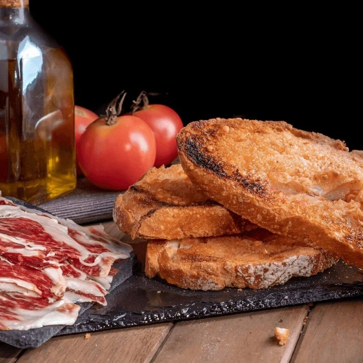 Tostada de pan con aceite de oliva y  finas lonchas de jamón ibérico 100% cortado a cuchillo